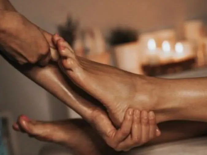 Massagem nos pés, com as mãos envolvendo o pé da cliente