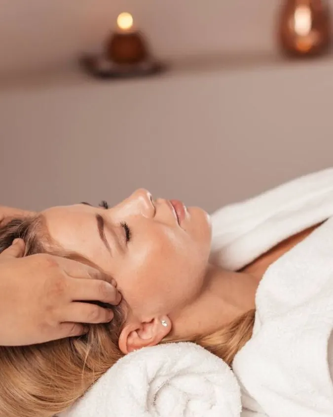 Mulher relaxada recebendo massagem na cabeça e no pescoço, deitada na maca