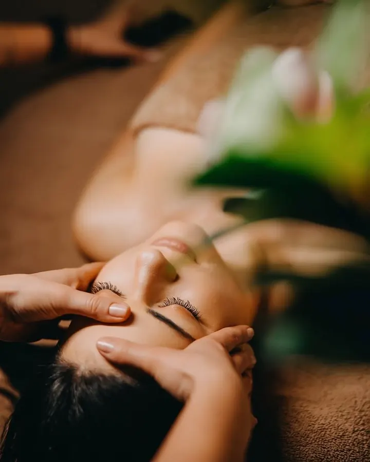 Cliente de olhos fechados recebendo massagem relaxante na cabeça, deitada na maca